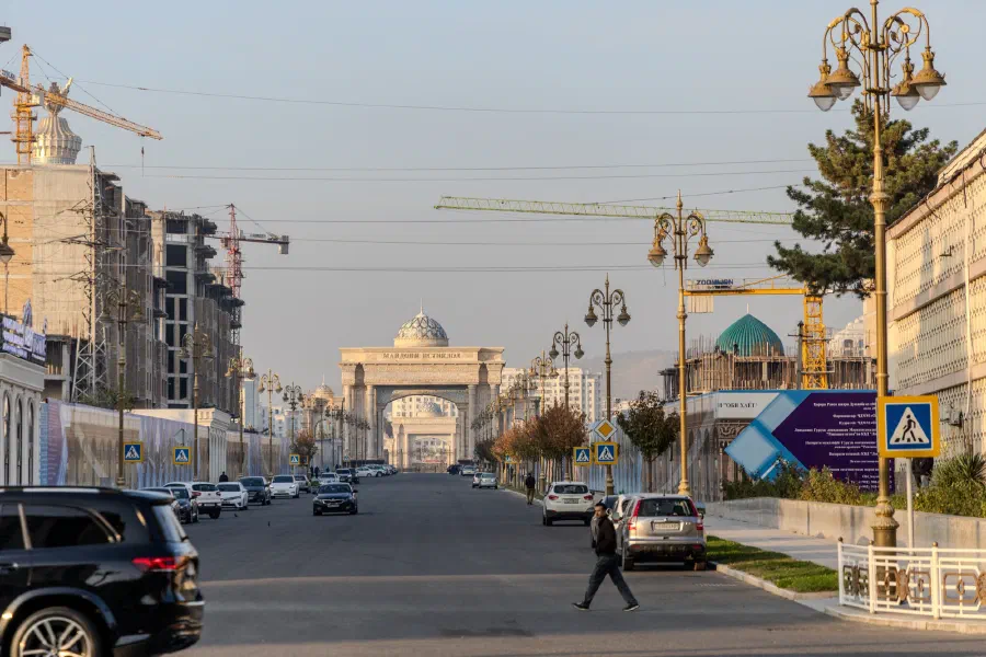 Широкий проспект с фонарями ведёт к монументальной арке и стройке с кранами