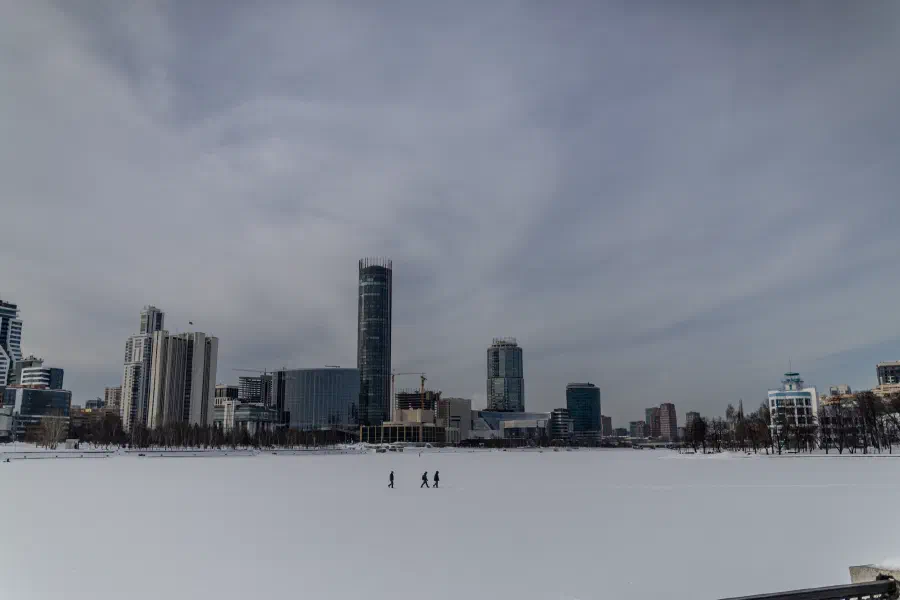 Панорама заснеженного города со стеклянной башней за руслом замёрзшей реки