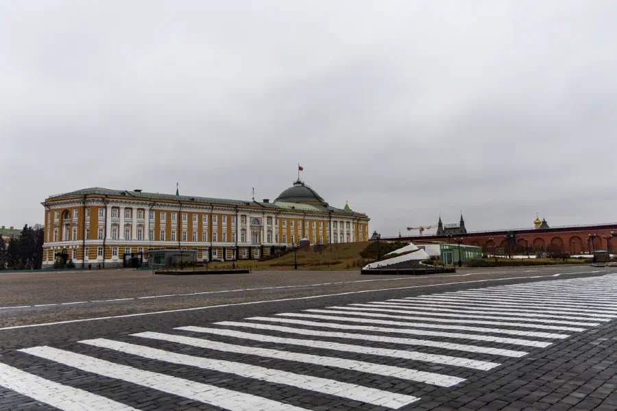 Классическое жёлтое здание с зелёным куполом на пустой мощёной площади в пасмурный зимний день