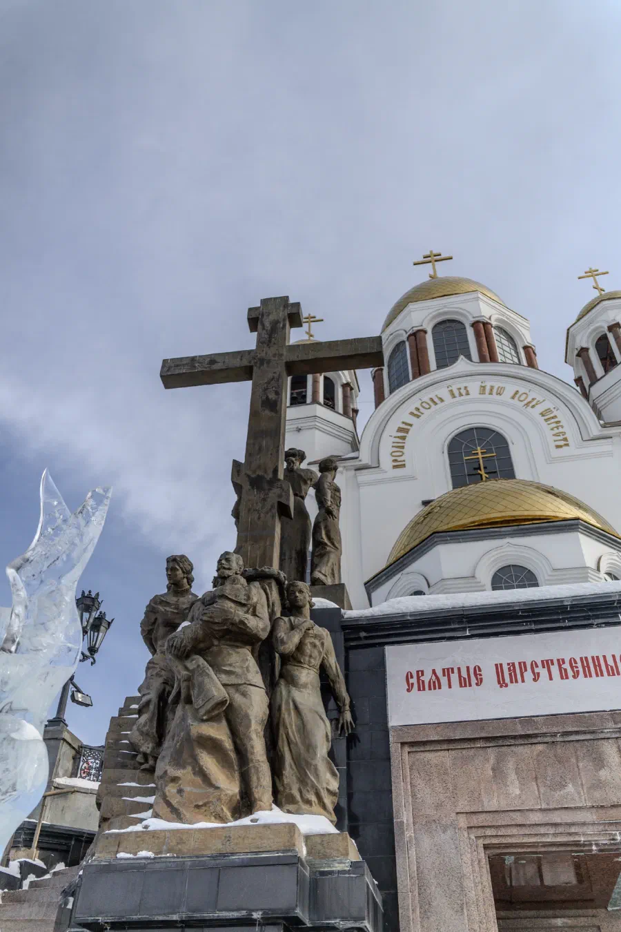Памятник с крестом и скульптурами перед собором с золотыми куполами в зимний день