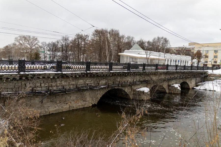 Старинный каменный арочный мост с коваными перилами через реку зимой